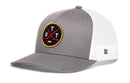 The Haka Hat Ottawa Hockey Trucker Hat | OTT X Snapback by Haka Hat features a gray and white design with a round black patch on the front, showcasing two crossed red hockey sticks and yellow “O T T” letters. This signature 5.0 trucker hat includes a mesh back, snapback closure, and a slightly curved brim.