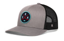 The Haka Hat Seattle Hockey Trucker Hat | SEA X Snapback is a gray and black trucker hat featuring a round front patch with crossed hockey sticks, the letters S E A, and a puck. This Seattle hockey hat by Haka Hat has a mesh back, snapback closure, and curved brim.
