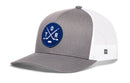 Introducing the Haka Hat Toronto Hockey Trucker Hat | TOR X Snapback: a gray and white mesh snapback cap from Haka Hat, styled in the classic Toronto hockey trucker design. It features a blue round premium embroidered patch with two crossed bats, a puck, and the letters T, O, and R. This hat comes with a slightly curved bill and a small logo tag on the side.