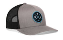 Haka Hat Utah Hockey Trucker Hat | UTA X Snapback: a grey trucker hat with a black mesh back and a circular patch featuring crossed hockey sticks and the letters U, T, and A in light blue.
