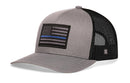 The Haka Hat Thin Blue Line Trucker Hat is a gray-black police tactical snapback featuring a mesh back and a front patch with a black and gray American flag and a single blue line.