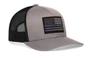The Haka Hat Thin Blue Line Trucker Hat is a gray-black police tactical snapback by Haka Hat, featuring a black-and-gray American flag patch with a single blue stripe on the front.