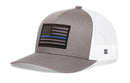 The Haka Hat Thin Blue Line Trucker Hat is a gray and white police tactical snapback with a black and white American flag patch featuring a blue stripe and a breathable mesh back.