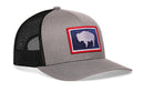 The Haka Hat Wyoming Flag Trucker Hat features a gray front, black mesh back, and a patch with a white bison on dark blue bordered in red, echoing the iconic Wyoming flag. This stylish snapback is from Haka Hat.