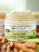 An open jar of Terrapin Ridge Farms Hatch Chile Cream Cheese Dip displays its creamy texture, surrounded by pretzels and a green veggie slice, highlighting the bold Southwest flavor of this Terrapin Ridge Farms favorite.