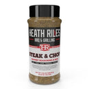 A bottle of Heath Riles Steak & Chop Seasoning by Heath Riles, a bold BBQ and steak seasoning with a black lid and a white label featuring red and black text, crafted for enhancing steak, pork, lamb, and burgers.