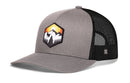 Introducing the Haka Hat Hexagon Mountain Trees Trucker Hat by Haka Hat—an outdoors snapback featuring a gray and black design with a hexagonal patch of mountains, trees, and a sunrise on the front. This hat includes a curved brim and breathable black mesh back for ventilation.