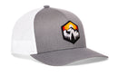 Introducing the Haka Hat Hexagon Mountain Trees Trucker Hat | Outdoors Snapback by Haka Hat—a gray and white adventure hat featuring a striking hexagon patch with mountain trees and a sunset on the front panel. The breathable mesh back ensures comfort, making this Haka Hat trucker hat the ideal choice for your next outdoor escape.