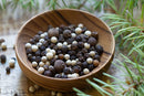 A wooden bowl filled with World Spice House Pepper Blend by World Spice, featuring aromatic Tellicherry black peppercorns and a mix of whole black and white peppercorns, sits on a wooden surface surrounded by fresh green rosemary sprigs.