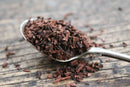 A spoonful of World Spice Honeybush herbal tea leaves rests on a rustic wooden surface, with some loose World Spice tea leaves scattered around.