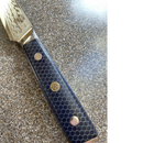 Close-up of the Spaceman Knives Interstellar Utility Knife by Spaceman Knives, featuring a patterned AUS-10 Damascus steel blade and a dark blue honeycomb-textured handle with three decorative rivets, resting on a speckled countertop.