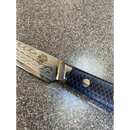 A close-up of the Spaceman Knives Interstellar Utility Knife by Spaceman Knives, featuring a patterned Damascus blade and a dark handle with a honeycomb design, resting on a speckled countertop.