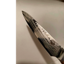 Close-up of the Spaceman Knives Interstellar Utility Knife blade, featuring its signature wavy Damascus patterns and the Spaceman Knives logo near the handle, set against a plain light background—showcasing exceptional craftsmanship.