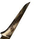Close-up of the Spaceman Knives Interstellar Boning Knife blade by Spaceman Knives, showcasing its polished Damascus steel with a wavy pattern and emblem near the handle. The blade rests on a white surface with ruler markings, emphasizing precise trimming.
