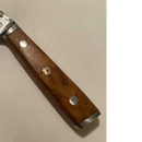 Close-up of the Spaceman Knives Interstellar Utility Knife handle, crafted from wood with silver rivets and a decorative metal pin, shown on a light-colored textured surface.