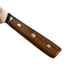 Close-up of the Spaceman Knives Interstellar Boning Knife handle, featuring smooth wood with two large metal rivets and a small circular emblem, resting on a beige surface.