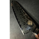A close-up of the Spaceman Knives Interstellar Chef Knife by Spaceman Knives, featuring a patterned AUS-10 steel blade and a round gold logo near the handle, set against a dark background.