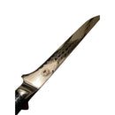 A close-up of the Spaceman Knives Interstellar Boning Knife’s Damascus steel blade, featuring the Spaceman Knives logo near the handle and held before an inch-marked ruler, perfect for precision trimming.
