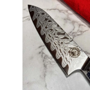 A close-up of the Spaceman Knives Interstellar Petty Chef Knife shows its intricate Damascus steel pattern on the blade, resting on a white marble surface with the Spaceman Knives logo near the handle.