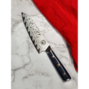 The Spaceman Knives Interstellar Petty Chef Knife by Spaceman Knives with a dark handle is displayed on a white marble surface beside a red cloth.