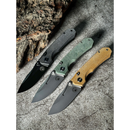 Three Spaceman Knives N1 EDC folding knives from Spaceman Knives, each with a textured Micarta handle in gray, green, and tan, are arranged side by side on a gray stone surface with rough tree bark behind them.