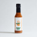 A bottle of Culture Hot Sauce Coconut Curry from Culture Hot Sauce, with a white label displaying an orange handprint and green text, stands on a plain light background. This hot sauce blends creamy coconut with the bold spices of Madras curry for a uniquely flavorful experience.