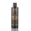 A black 7.5 oz (222 mL) bottle of The Immaculate Beard Body Wash by The Immaculate Beard, labeled “DARK” and featuring paraben-free scents of tobacco blossom, caramel, honey, and rose, stands on a reflective surface.