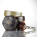 A wrapped bar of The Immaculate Beard Shave Soap rests next to two rustic bowls, while a safety razor in a brown leather case is set in front—all arranged on a white background to capture the timeless ritual of a traditional hot shave, making this Shave Gift Set from The Immaculate Beard the perfect gift.