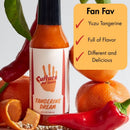 A bottle of Culture Hot Sauce Tangerine Dream by Culture Hot Sauce is displayed among fresh tangerines and red peppers. Beside it sits a checklist: “Fan Fav - Yuzu Tangerine, Full of Flavor, Different and Delicious,” highlighted with bold red checkmarks. This vibrant citrus hot sauce masterfully blends tangy tangerine with zesty yuzu for a truly unforgettable flavor experience.
