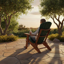A person relaxes in a Kanyon Living Kanyon Poly Folding Adirondack Chair in Dark Green and Cedar Wood on a stone patio, enjoying a drink and the peaceful sunset garden, surrounded by trees and warm golden light.