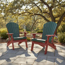 Two Kanyon Living Kanyon Poly Folding Adirondack Chairs in Dark Green & Cherry Wood sit on a stone patio under string lights, surrounded by lush greenery and trees—a charming spot to relax with sustainable outdoor furniture.