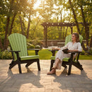 A woman relaxes in a Kanyon Living Kanyon Poly Folding Adirondack Chair in Lime Green and Black on a sunny patio, sipping from a mug and reading, with outdoor seating made from recycled poly lumber and trees behind her.