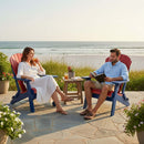 Two people relax on a beachside patio in Kanyon Living Kanyon Poly Folding Adirondack Chairs in Red and Blue, enjoying drinks and a book. Ocean views, lush plants, and flowers complete the tranquil scene.