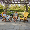 A man and a woman relax in Kanyon Living’s Kanyon Poly Folding Adirondack Chair Yellow and Cedar Wood under a pergola with wisteria, smiling with drinks as they enjoy blooming hydrangeas and inviting outdoor seating.