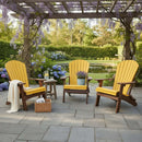 Three Kanyon Living Poly Folding Adirondack Chairs in Yellow and Cedar Wood are set on a stone patio under a pergola with wisteria, complemented by a small table with lemonade, a blanket, and basket near the garden and pond.