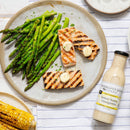 A plate with grilled asparagus, two pieces of grilled salmon topped with butter, corn on the cob, and a bottle of Terrapin Ridge Farms Lemon Honey Vinaigrette from Terrapin Ridge Farms on the side.