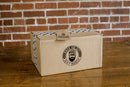 A Manly Cans 50 Cal CANivore Meat Gift Can by Manly Cans sits on a wooden table with a brick wall backdrop, decorated with a tag and tape—perfect for gifting beef jerky.