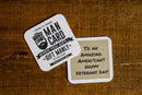 Two coasters on a wood surface: one promotes Manly Cans BBQ Gift Can as the perfect BBQ gift, while the other reads “To an amazing American!! Happy Veterans Day!”.