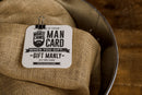 The Manly Cans 30 Cal CANivore Meat Gift Can comes in a metal tin with burlap lining, clipped to a “Man Card” square card—perfect for gifting beef jerky. Features the Manly Cans beard logo on a wooden surface.