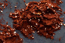 A scattered heap of World Spice Mayan Cocoa—a reddish-brown powder intermingled with chunks from World Spice—blends with small, white oval seeds across a dark gray surface.