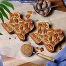 Two Medium Texas Pecan Cakes from Texas Pecan Cakes, each infused with authentic Texas flavor and crowned with pecan halves, rest on parchment paper beside a bowl of whole pecans, a metal measuring cup filled with brown sugar, and a green leaf. This 2-Pack serves 10-12 people.