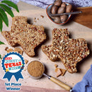 Two Medium Texas Pecan Cakes shaped like Texas from Texas Pecan Cakes are arranged on a wooden board, alongside a bowl of pecans with a nutcracker, a measuring cup filled with brown sugar, and a blue 1st Place Winner ribbon from H-E-B Quest for Texas Best—showcasing authentic Lone Star flavor. Perfect for anyone who loves classic pecan cake or wants to celebrate the rich tradition of the Texas Pecan Cake. This 2-pack serves 10-12 people.