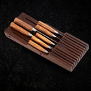 A set of kitchen knives with light wooden handles is neatly arranged in a Messermeister In-Drawer Knife Holder - 11 Slot by Messermeister, placed on a textured black surface.