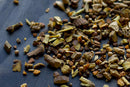A close-up of assorted dried spices and herbs from World Spice Mystic Licorice Tea, scattered on a dark surface, featuring pieces of bark, seeds, and roots in rich brown and golden tones—perfect for enjoying a warming cup or blending your own licorice root tea with World Spice.