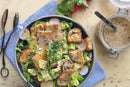 A bowl of salad with lettuce, radish slices, croutons, and black sesame seeds sits on a blue napkin. A jar of World Spice Nigella Caesar dressing by World Spice and utensils are nearby. Radishes are seen at the top of the image.