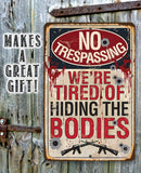 The No Trespassing Tired of Hiding The Bodies - Metal Sign by Lone Star Art features bullet holes, blood spatters, and gun images—perfect dark humor decor or a hilarious gift!.