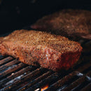 A thick, seasoned steak is sizzling on the grill, boasting visible grill marks and a smoky backdrop, all elevated by Dead Rooster Co.’s Old Timers All-Purpose Dry Rub that brings out robust flavors in every bite.