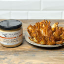 A jar of Terrapin Ridge Farms Onion Blossom Horseradish Dip from Terrapin Ridge Farms sits beside a crispy blooming onion appetizer on a light surface with a white tile background.