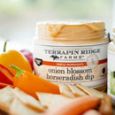 An open jar of Terrapin Ridge Farms Onion Blossom Horseradish Dip sits with dip on the rim, surrounded by vibrant bell peppers and crackers, highlighting its steakhouse-inspired flavor.