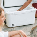White 50-quart cooler by Bison Coolers with an open lid, standing on a stone surface near two people.